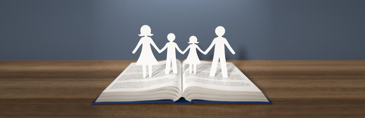 Scherenschnitt einer Familie, die auf einem Buch stehen.